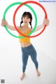 A woman in a yellow top and blue leggings holding two hula hoops.