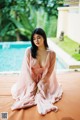 A woman in a pink robe sitting by a pool.
