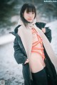 A woman in a black jacket and orange bikini standing in the snow.