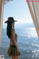 A woman in a leopard print bikini and a hat standing by the water.