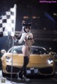 A woman in a bikini holding a checkered flag next to a car.