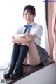 A woman in a school uniform sitting on a window sill.