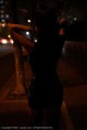 A woman in a black dress standing on a sidewalk at night.