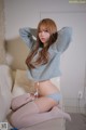 A woman sitting on a white couch wearing a blue sweater and stockings.