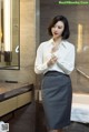 A woman in a white shirt and gray skirt standing in a bathroom.