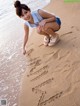 A woman kneeling down on the beach writing in the sand.