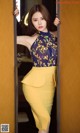 A woman in a yellow skirt leaning against a wall.