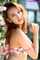 A woman in a bikini posing in front of flowers.