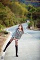 A woman in a striped dress and fur coat posing on a road.